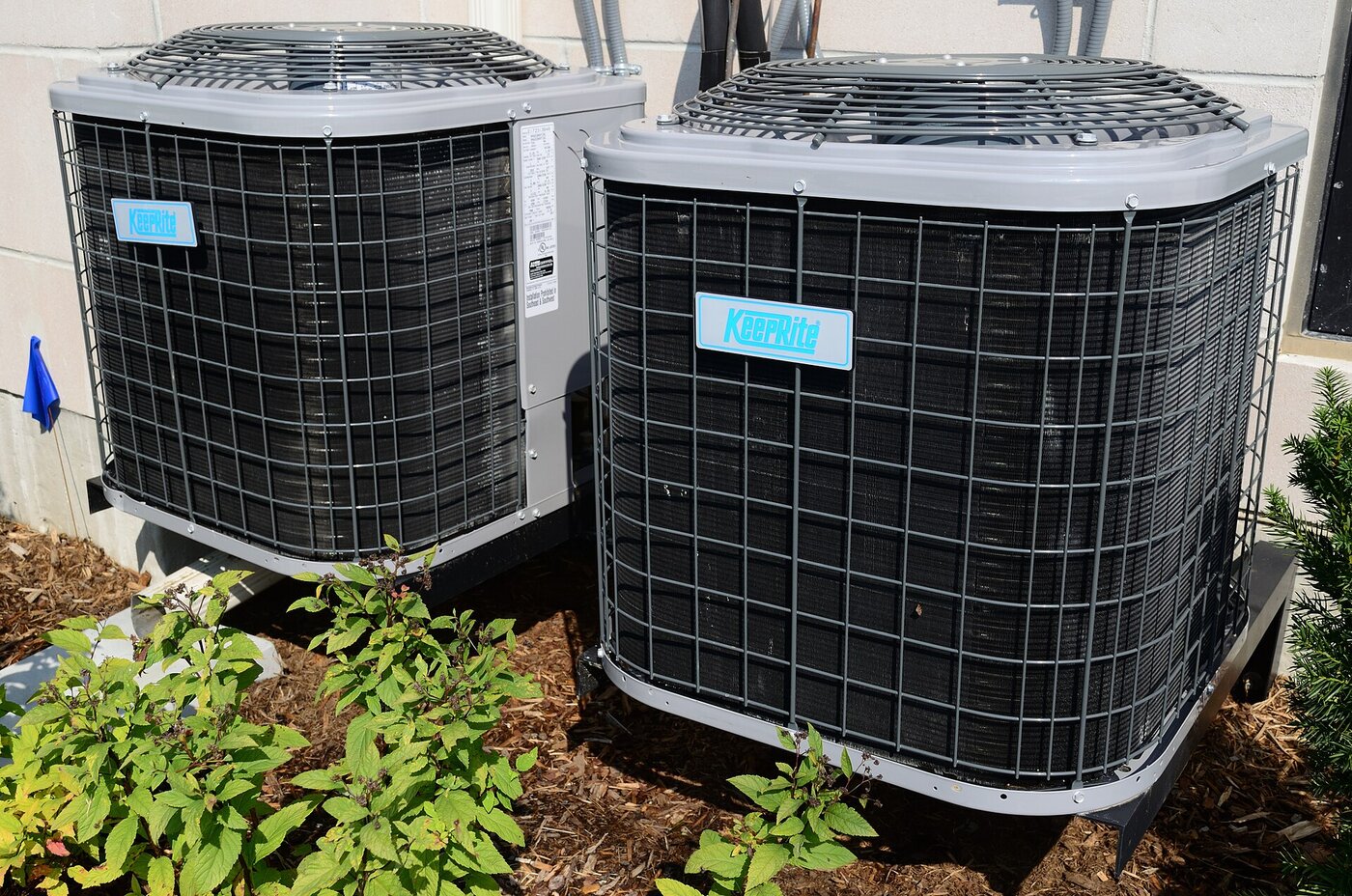 Two residential outdoor AC condensers on stands beside a house